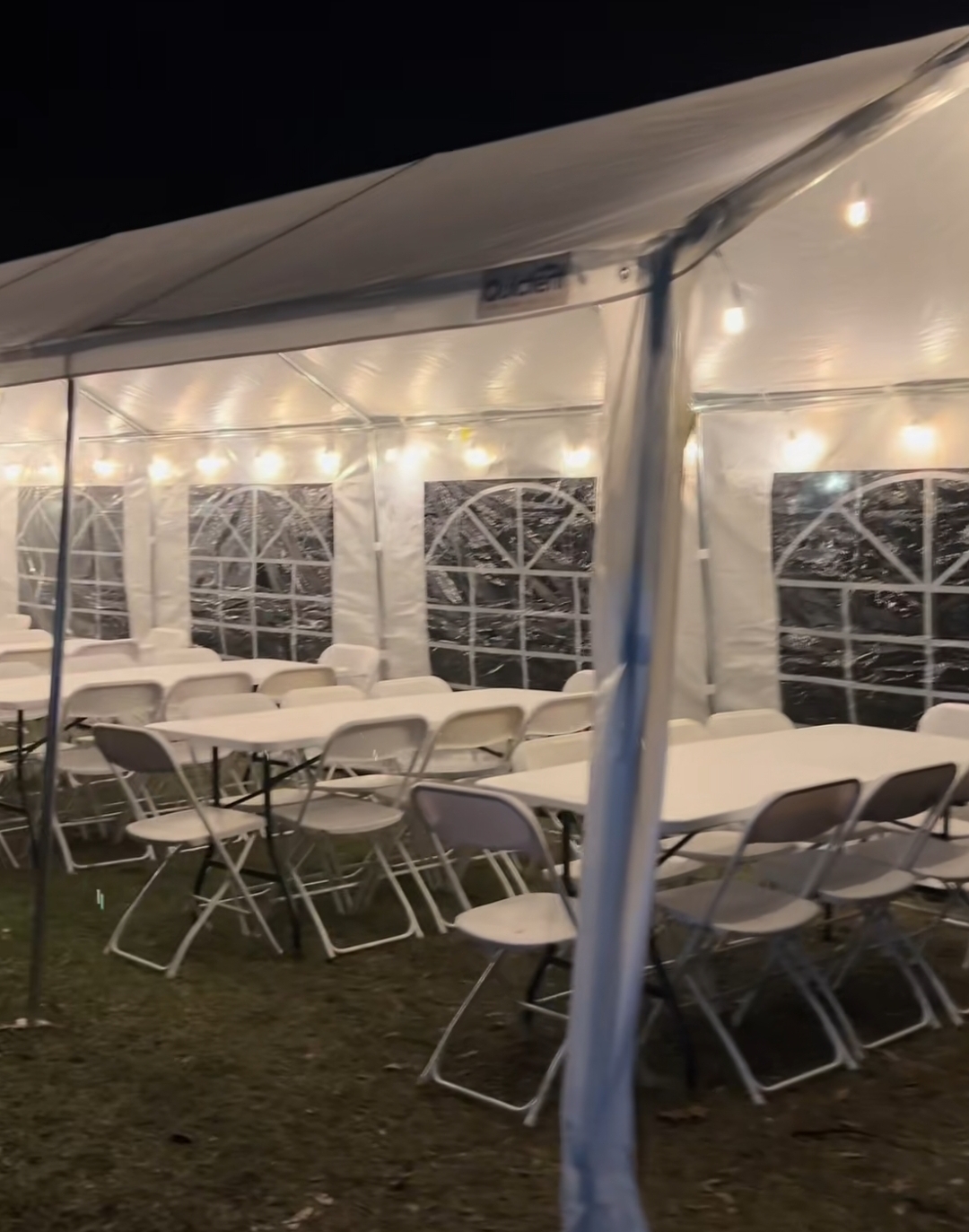 Inside a lit tent at night with long tables and white folding chairs