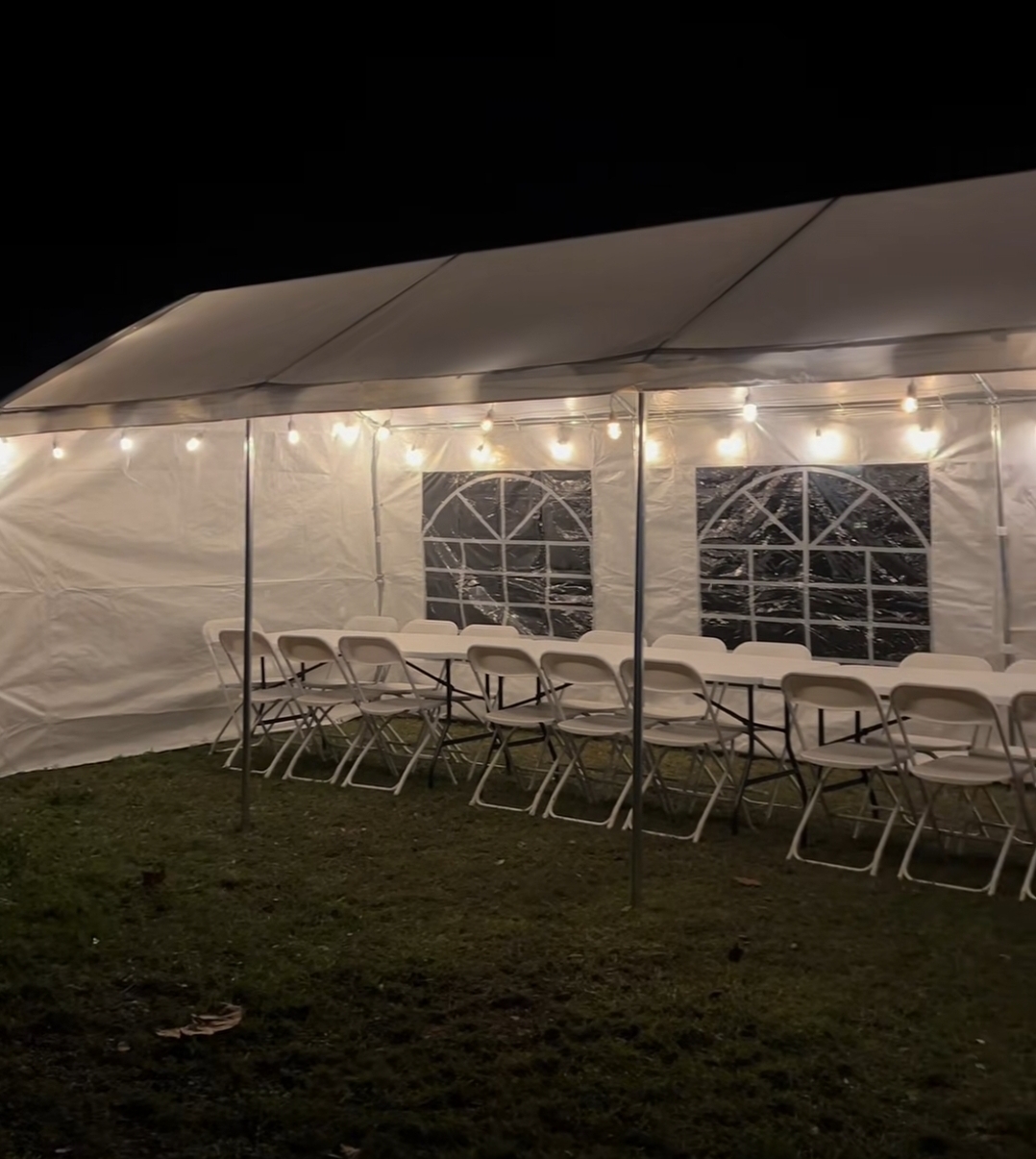 Long banquet tables with white chairs inside a tent with window sidewalls