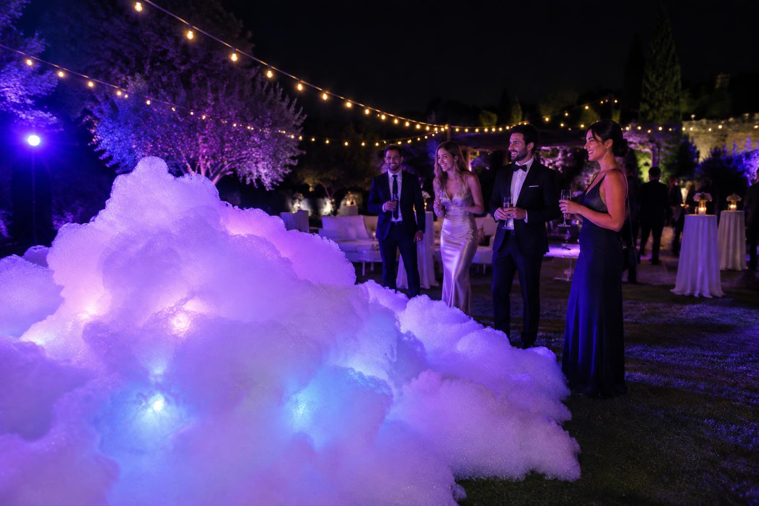 Glowing foam under purple lights at an upscale adult night celebration with string lights and dressed-up guests